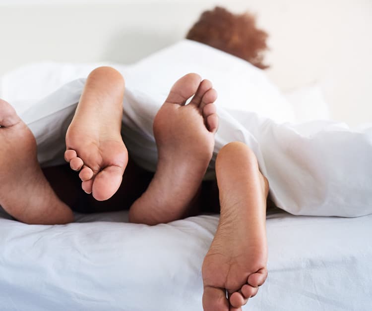 Two sets of feet at the end of a bed covered with blankets
