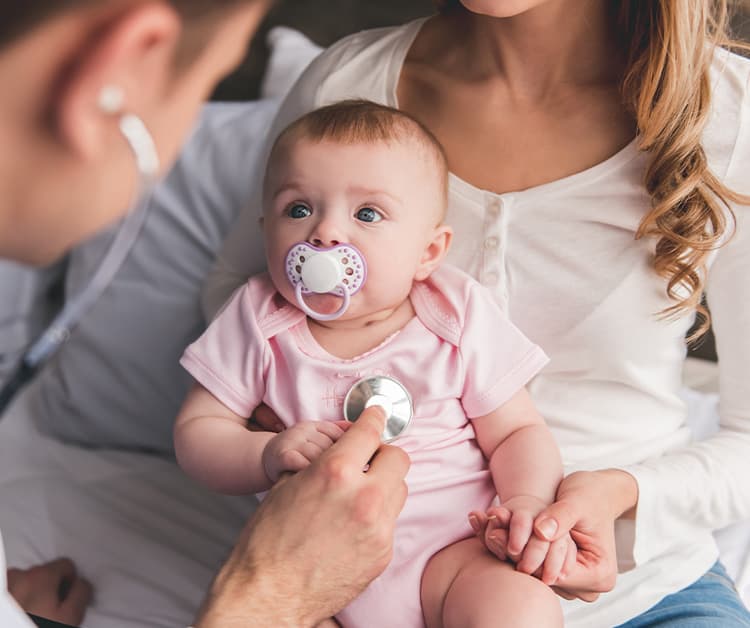 Baby with a pacifier being held by her mother while a pediatrician listens to her chest