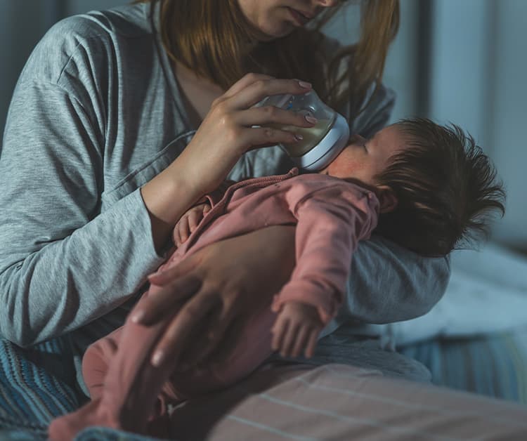 A mother bottle-feeding her baby during the night