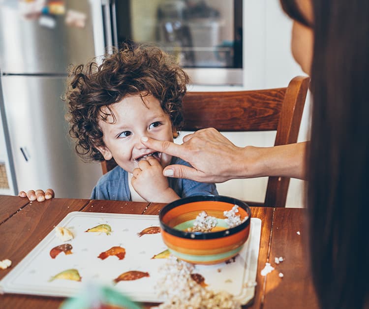 Toddler boy and his mom sitting at the table with a bowl of food