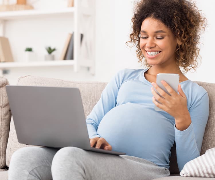 Pregnant woman sitting on the couch using her laptop and phone