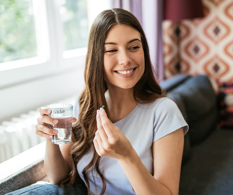 Smiling woman holding a glass of water and a vitamin