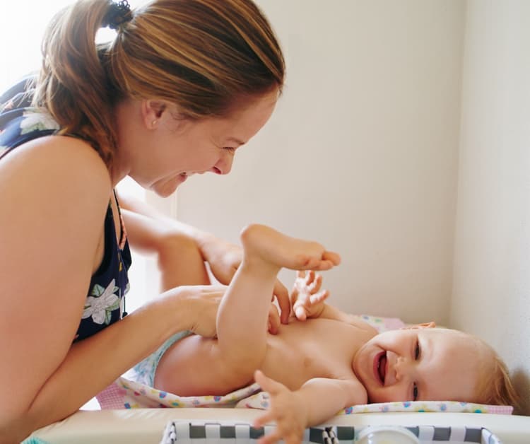 Smiling mom changing happy baby's diaper