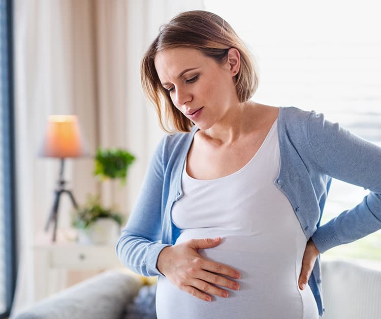 Pregnant woman holding her bump looking like she is in some discomfort