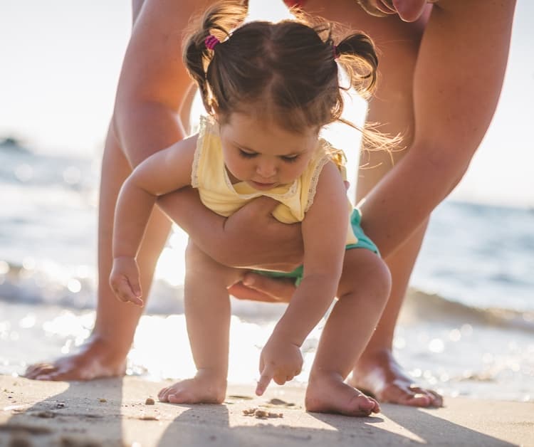Toddler girl playing in the sand with parent