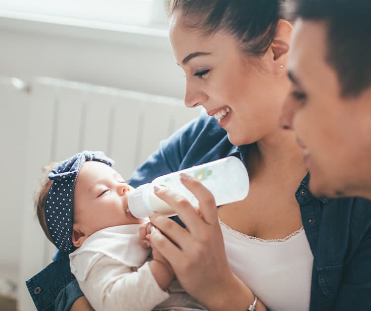 Mom feeding baby a bottle with dad smiling close by