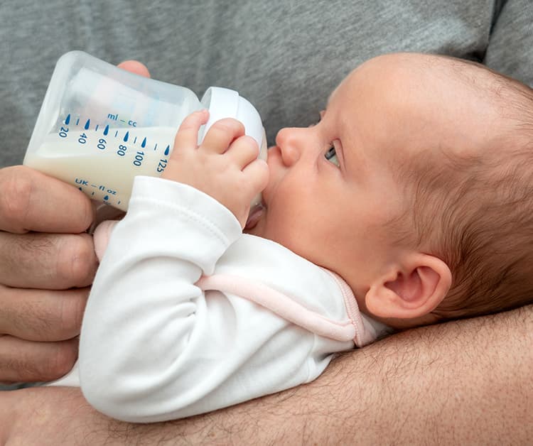 Parent sitting down and bottle feeding their baby