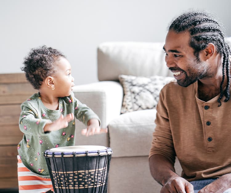 Toddler banging on drums and looking at dad