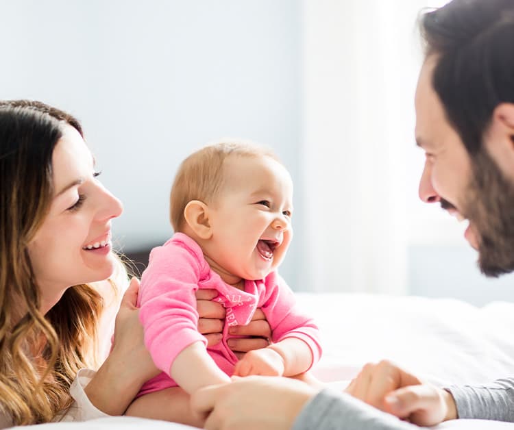Dad and mom smiling with baby on the bed