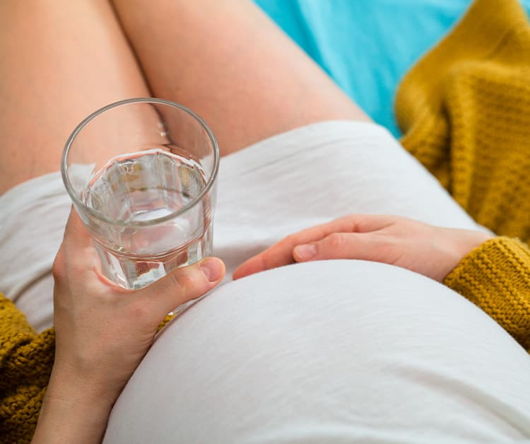 Pregnant mom holding her belly and holding a glass of water
