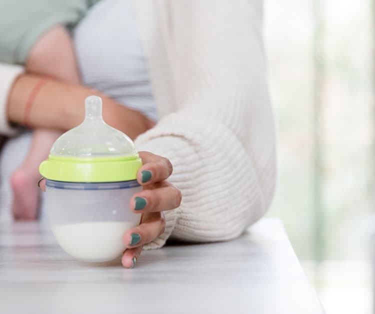 Mom reaching for bottle on the counter with baby in her arms