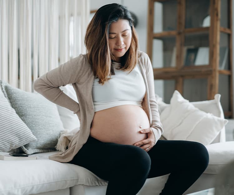 Pregnant woman sitting on the couch holding her belly bump and back