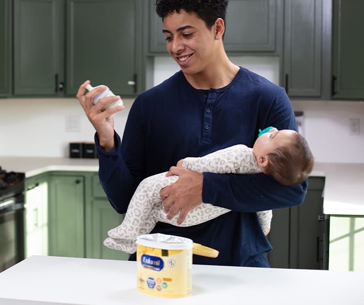 Dad checking bottle while cradling baby