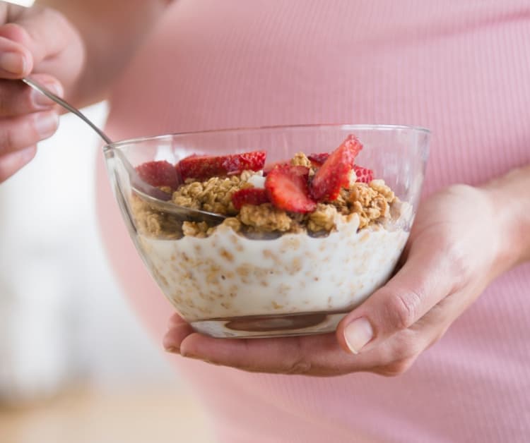 Pregnant mom eating yogurt with granola and fruit