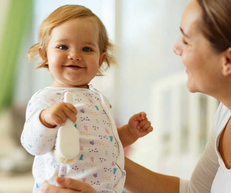 Baby girl holding a hairbrush and her mom is holding her